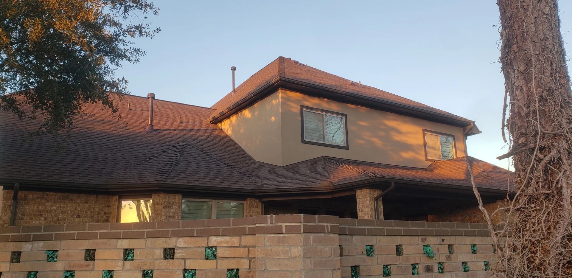 The sun sets beautifully over a large multi-level home that showcases brand new shingles after a completed residential roof replacement.