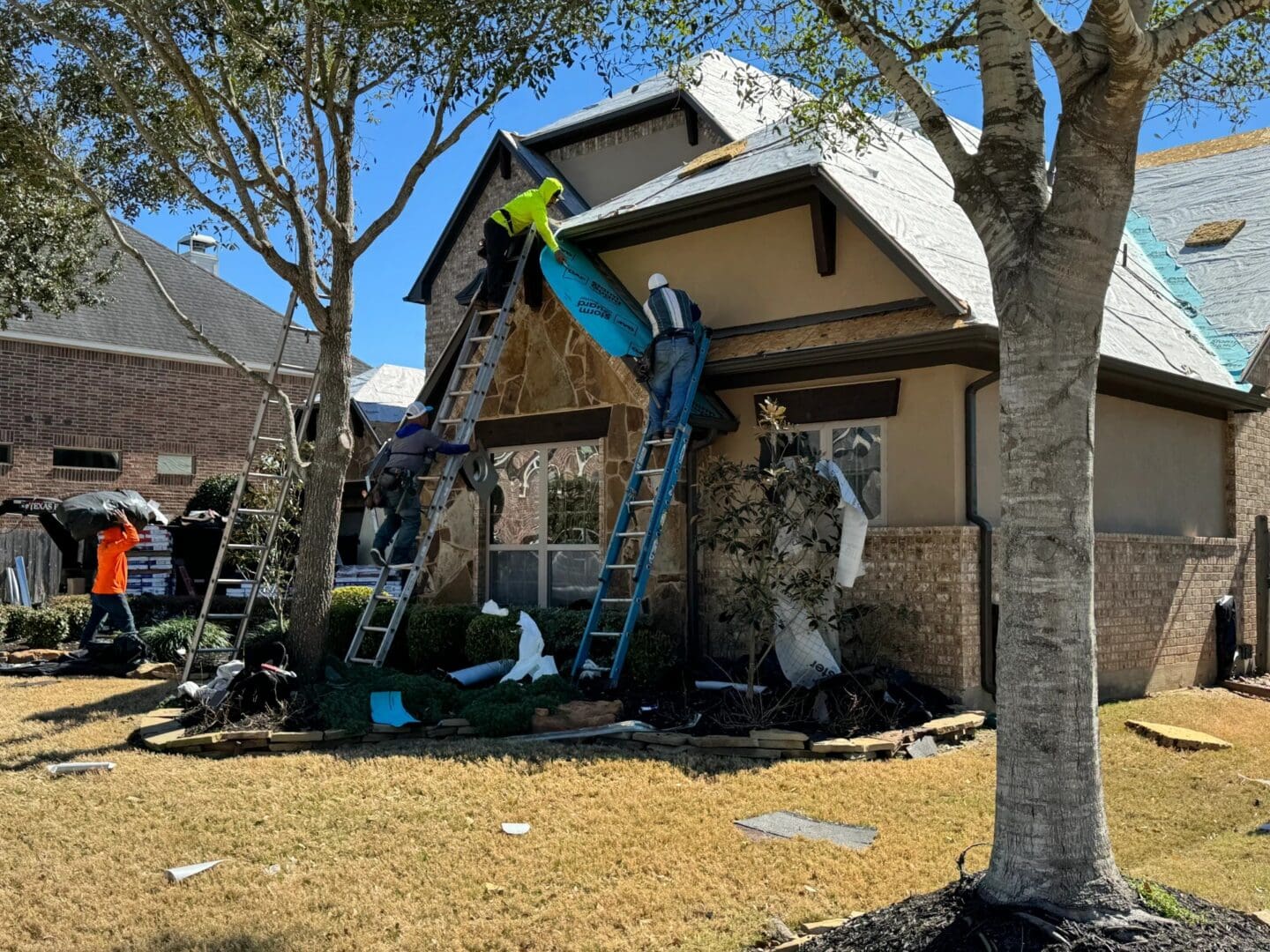 A team of contractors uses ladders to install protective underlayment on a home during a residential roof replacement.